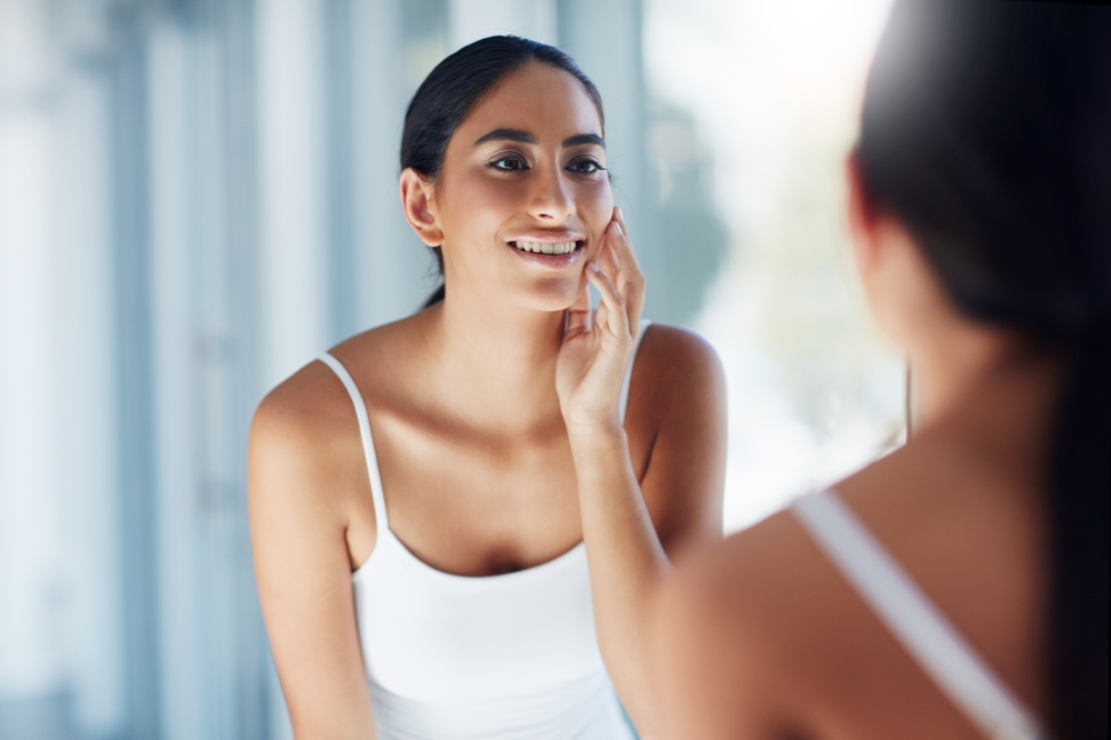 Woman smiling at her reflection, touching her face, post-SkinPen microneedling treatment for smoother skin.